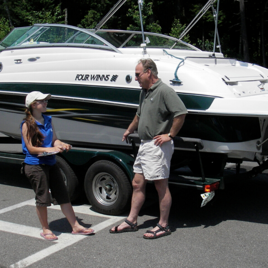 Two people standing in front of a speed boat having a conversation