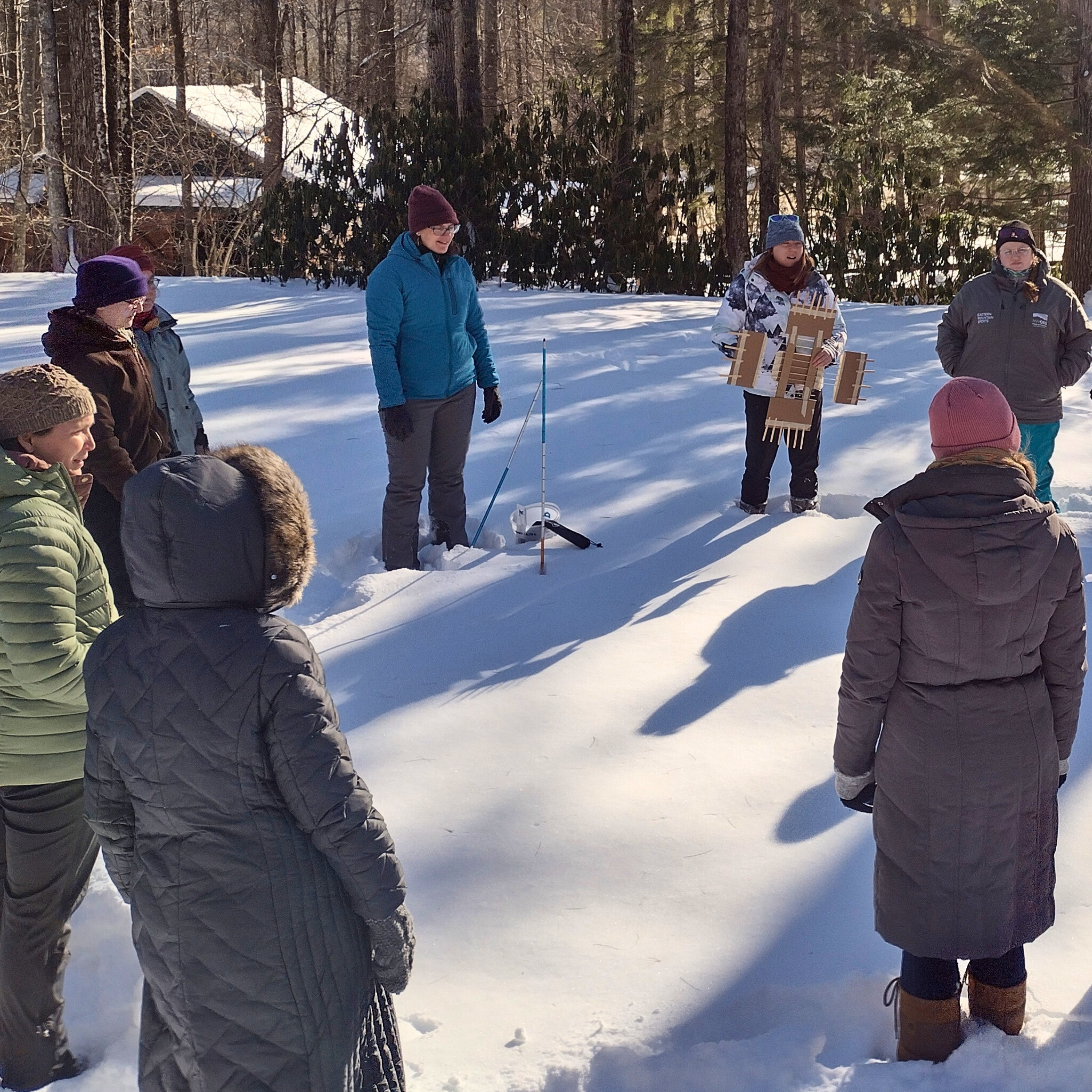 Adults in a snowy field measuring snowpack.