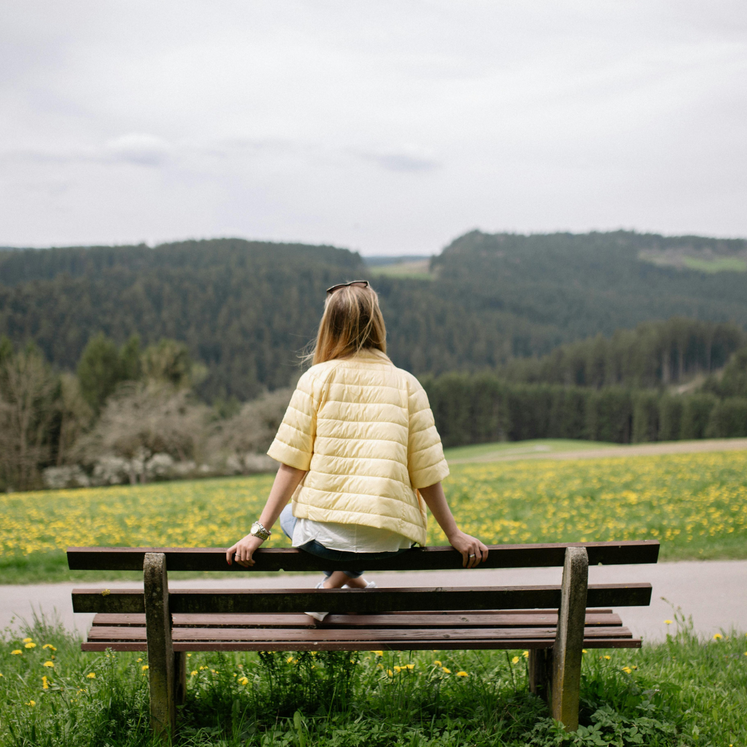 A woman sitting on a bench looking towards some mountains.