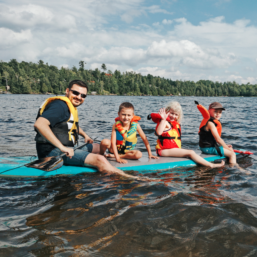 A smiling family riding a paddleboard together on a lake.