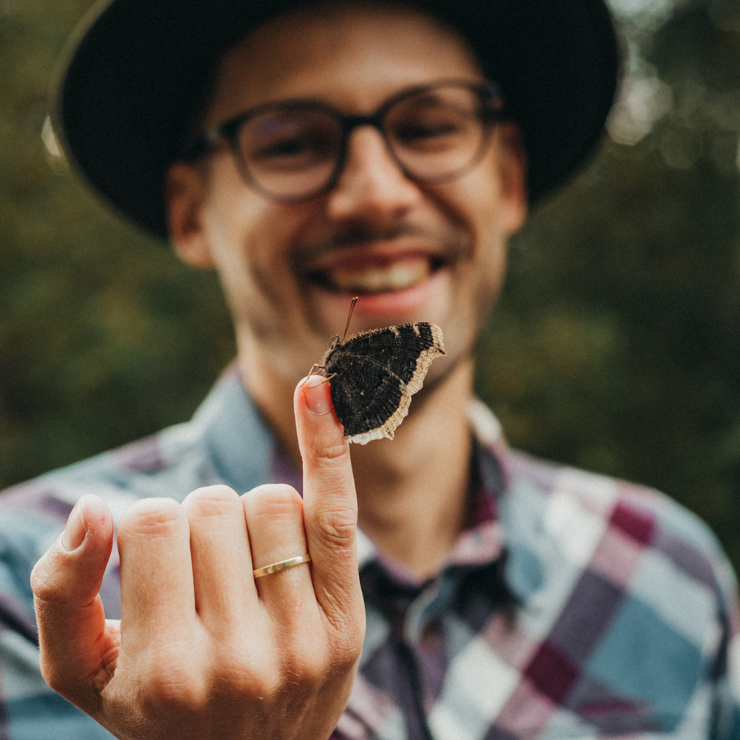 a smiling man looking at a butterfly resting on his fingertip